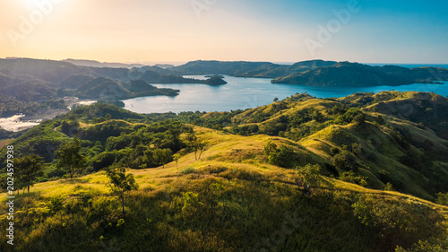 Quadro su tela Drone shot of golden savanna hills bordering a quiet tropical bay under a warm sunset sky in Riung 17 Islands National Park