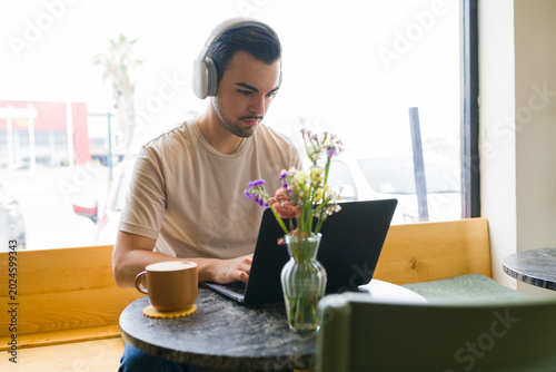 Photos Young man concentrating on laptop, working remotely from a coffee shop with head