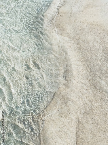Photography Top view of crystal clear water ripples on fine white sand beach, abstract nature background