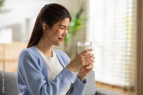 Tableau sur toile Young asian woman unhappy holding glass of water with grimace feeling disgusted by unpleasant taste sitting home