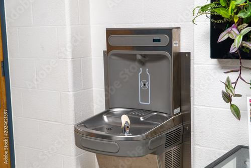 Foto Modern stainless steel water fountain and bottle filling station with a 'Bottles Saved' counter against a white brick wall, promoting eco-friendly hydration and plastic waste reduction