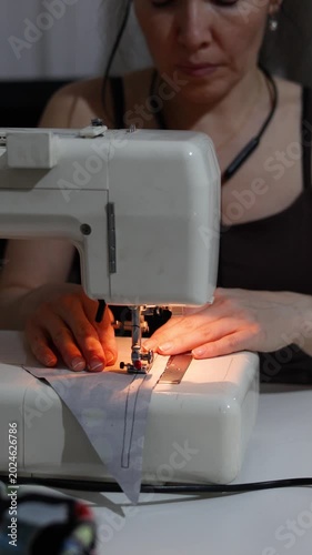 Focused hands guide blue fabric under a sewing machine's needle, creating even, perfect stitches. The close-up emphasizes the precision and craftsmanship of the stitching process.