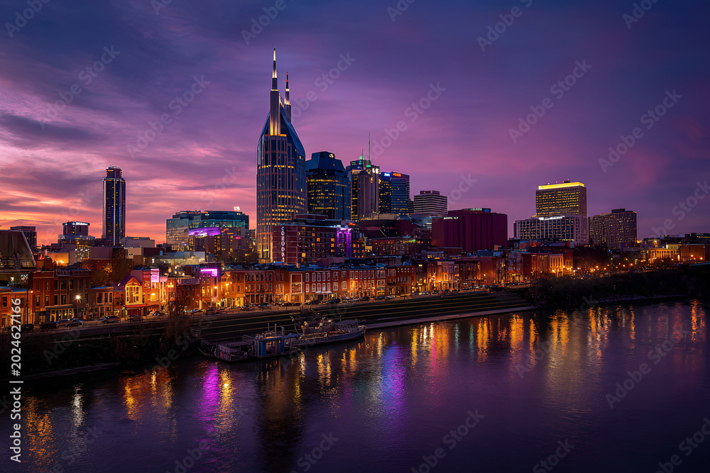 Fototapeta premium A vibrant dusk cityscape reflects in a calm river. Modern skyscrapers and historic buildings gleam under a colorful sky