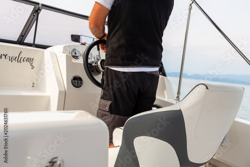 Man steering a modern motorboat with a sleek dashboard and comfortable seating, calm waters of Lake Garda visible in the background