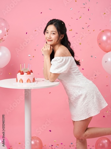 Young woman with birthday cake at party with pink balloons