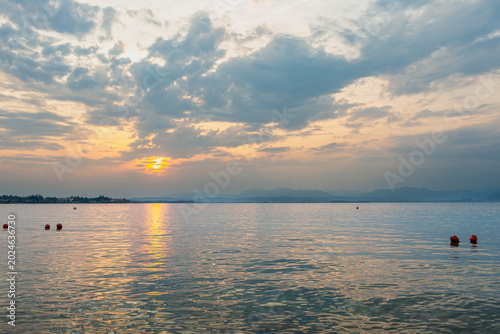 Scenic lakeside promenade lined the shores of Lago Garda in Italy, with a calm water surface reflecting the sky and distant hills.