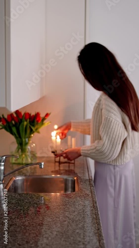Vertical video of an unrecognizable woman lighting candles in a moody dark kitchen creating a cozy home atmosphere