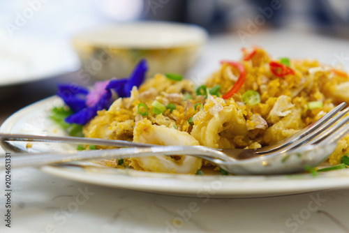 Stir-fried squid with salted egg yolk served on white plate. Authentic Thai seafood dish, delicious calamari with rich yellow sauce in restaurant.