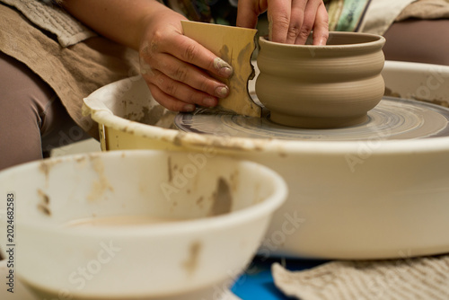 Artisan hands molding a tall ceramic vase on a spinning pottery wheel in a studio.