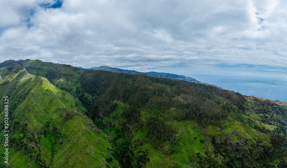 Naklejka premium Aerial drone view of the Madeira coastline with steep cliffs, Atlantic Ocean, and natural landscape. Calm travel scene with typical Portuguese island scenery.