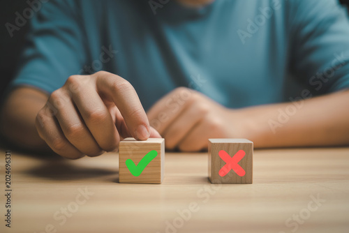 Person choosing between wooden cubes with green check mark and red cross symbol representing decision making.
