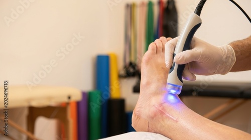 Physical therapist uses therapeutic laser device on patient's ankle with surgical scar