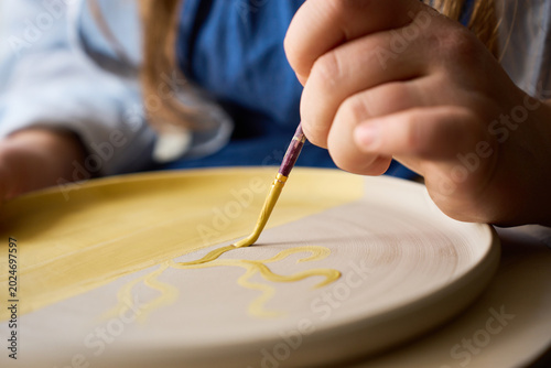 Professional ceramicist painting decorative motifs on a raw clay plate with yellow underglaze.