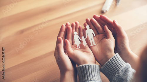 Hands cupping fragile paper cutout of family showing protection and care for loved ones on wooden background.