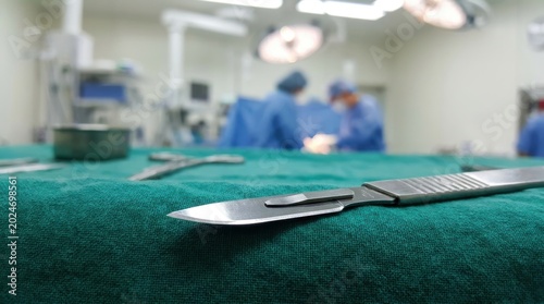 Surgical scalpel resting on a green cloth with medical professionals in blurred background
