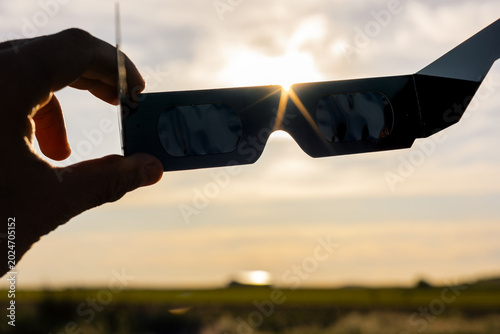 Billede på lærred Hand holding solar eclipse glasses, sun shining through optical filters for safe