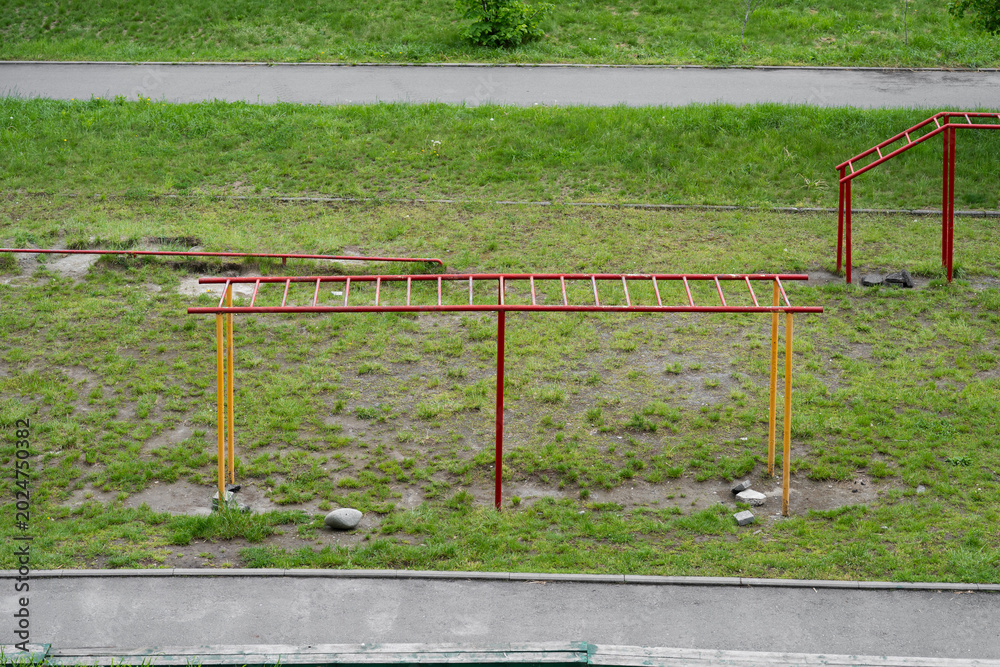 Fototapeta premium High-angle shot of outdoor metal monkey bars and sports equipment on a green grass field next to a walkway.