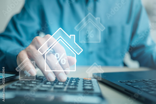 Tableau sur toile Hand using calculator with mortgage icons beside a laptop, representing home loan calculation, interest rates, monthly payments, housing finance, and refinancing decisions