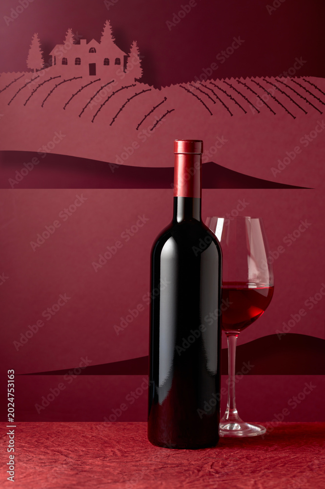 Obraz premium Bottle and glass of red wine on a red background.