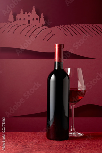 Bottle and glass of red wine on a red background.