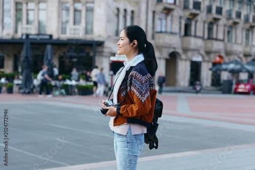фотографія Woman with camera on a city street, wearing a patterned jacket and backpack, urb