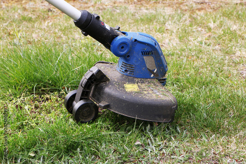 Slika na platnu A hand-held battery-powered grass trimmer is used to mow the grass