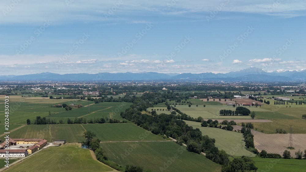 Fototapeta premium A sweeping aerial view showcases a vibrant green countryside, dotted with farms and lush fields, stretching towards a distant city skyline under a clear blue sky.