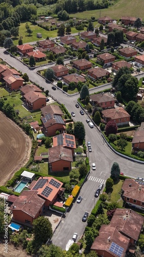 Aerial View of a Suburban Neighborhood: A high-angle drone shot captures a neatly arranged suburban community, showcasing rows of houses with tiled roofs and solar panels.