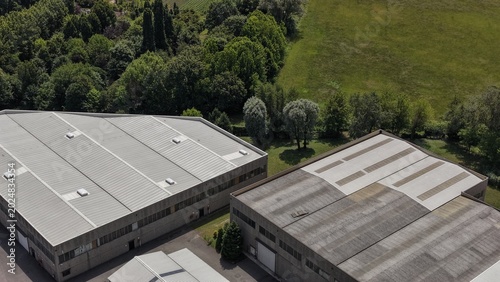 Industrial Complex in Green Landscape: An aerial view showcases a modern industrial complex with several warehouses, nestled amidst lush green fields and trees.