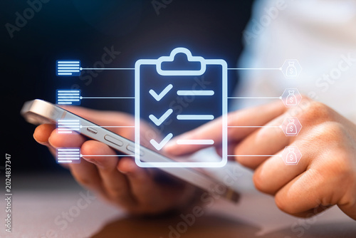 Fotografie Mobile phone user checking tasks and managing lists at a desk during a workday