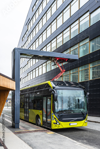 An electric city bus is charging at a charging station in Trondheim, Norway. Vertical.