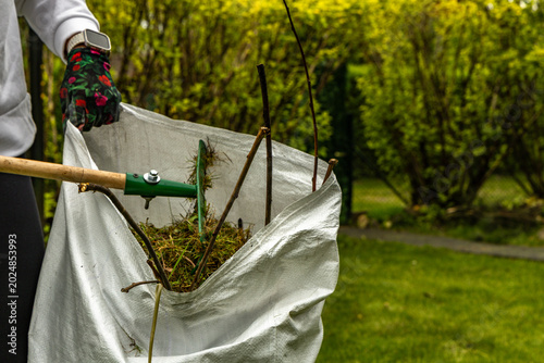 Female Gardener Raking Cut Branches and Leaves into White Garden Bag