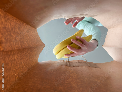POV from inside a brown paper bag of person packing fresh yellow bananas for grocery shopping