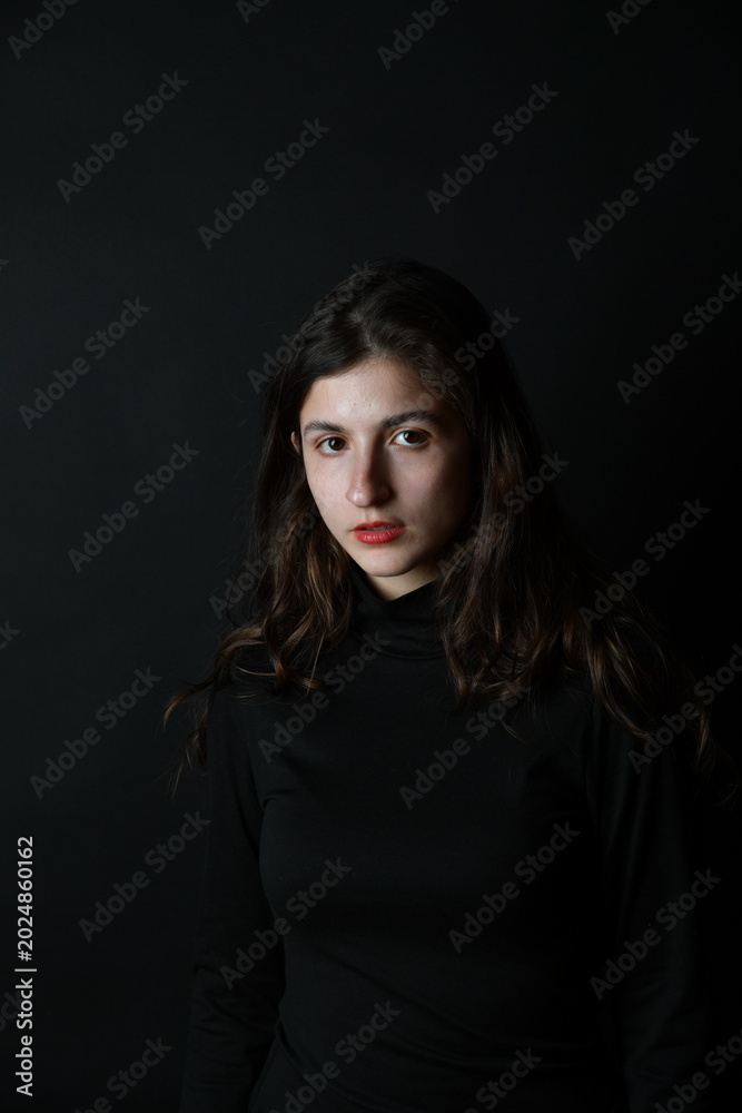 Naklejka premium Junge Frau im dunklen Rollkragenpullover vor schwarzem Hintergrund – ruhiges Fine-Art-Porträt mit melancholischer Stimmung und minimalistischer Ästhetik. Viel copyspace und copy space.