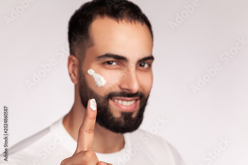 Foto Man showing moisturizing cream on fingertip for skincare while having product on