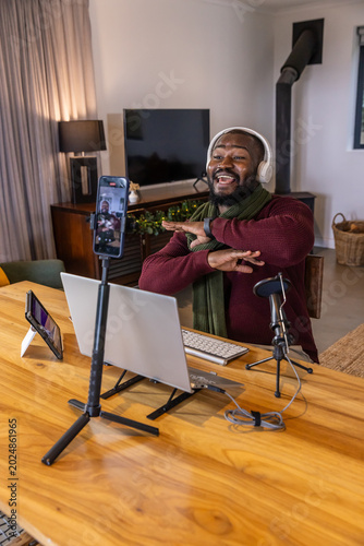 African American man recording at wooden table at home with phone and mic wearing maroon sweater