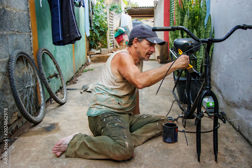 Foto Middle aged man restoring and painting a bicycle frame outdoors in a modest residential alley while a cat rests in the background