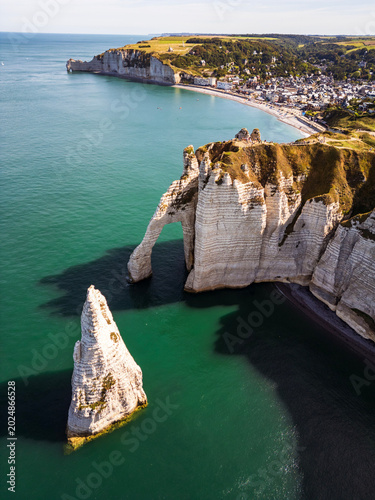 Aerial drone view of Etretat white chalk arch and needle rock with turquoise water and seaside town, Normandy