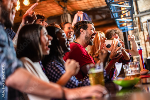 Side view of a group of excited friends celebrating a soccer goal at a pub bar counter.