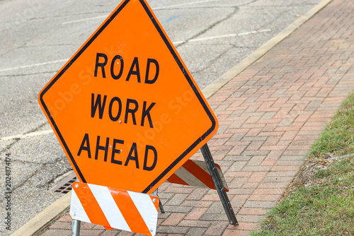 Road work ahead warning sign on sidewalk near street construction area