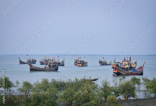 Traditional wooden fishing boats anchored in calm blue sea water near green mangrove coast of Teknaf Coxs Bazar Bangladesh beautiful tropical maritime landscape background
