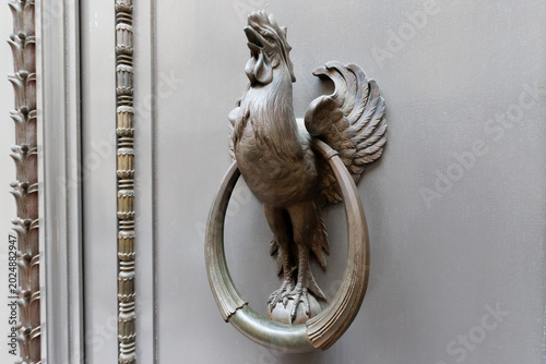 Detailed view of an ornate bronze Gallic rooster door knocker on a classical Parisian building, with a decorative carved stone pilaster visible to the left. Paris. France.