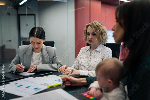 Business meeting with working mother holding baby in office conference room. Work life balance and modern parenting