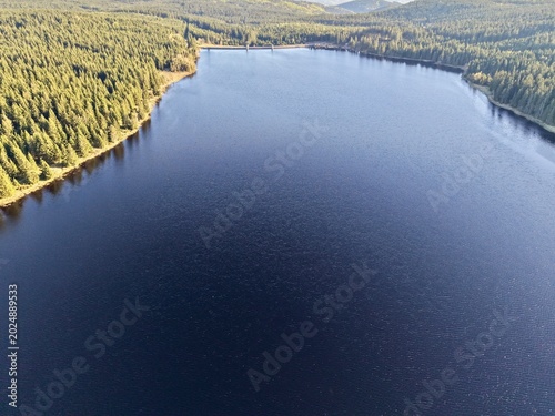 Fotografi Aerial perspective shows tranquil dark blue water and untouched forested shoreli