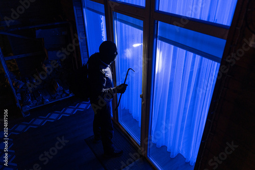 Foto Man with crowbar standing outside looking through window to break into house at