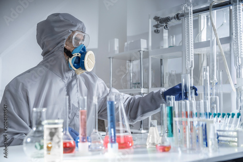 Scientist wearing full protective suit and respirator working with chemical glassware in a laboratory with hazardous substances
