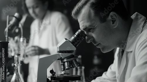 Profile of a scientist using a microscope in a vintage laboratory. Monochrome historical footage. First and Second World War science and medicine concept