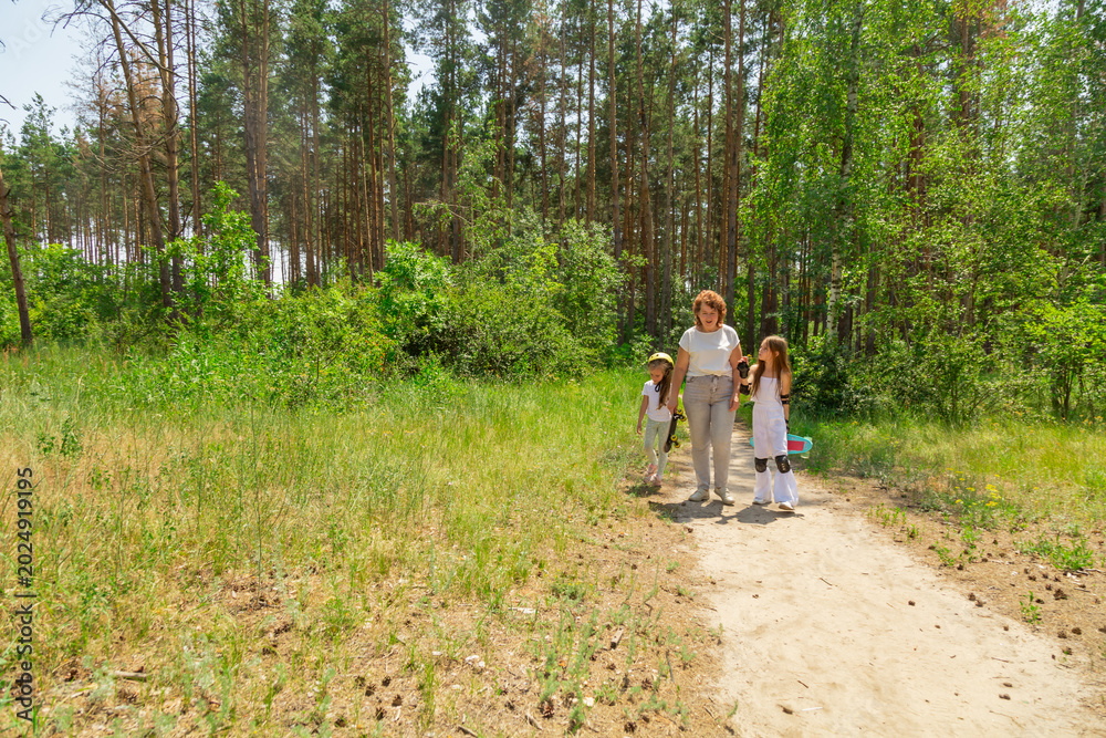 Fototapeta premium Grandmother and children walking with skateboards in the forest.