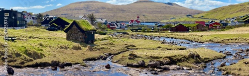 Panoramic view of Sandavagur village on the south coast of Vagar island with red-roofed church and mountains, Faroe Islands