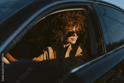 Foto Lifestyle woman drives a car with retro film color, wearing sunglasses and curly hair, warm golden light on her face, confident mood, urban roadside scene